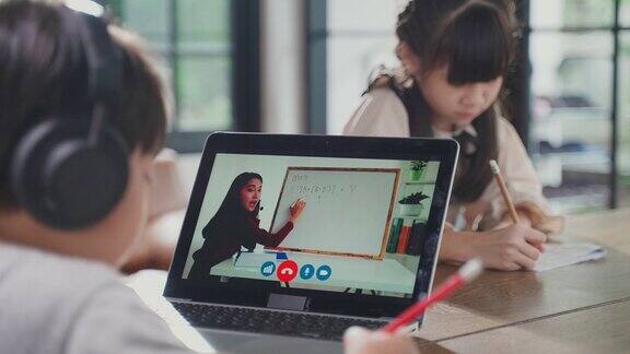 由于冠状病毒大流行亚洲小男孩通过数字远程互联网会议从学校老师那里学习在线课程孩子看着电脑笔记本电脑屏幕那个女人在教书