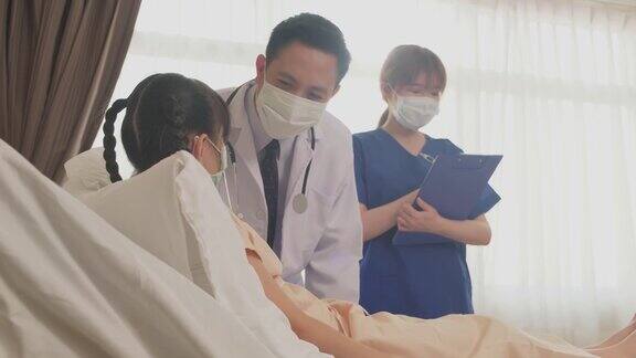 亚洲医生在康复室的床上用听诊器测量小孩的心率冠状病毒大流行期间戴口罩的男女检查女童年轻的护士和孩子说话