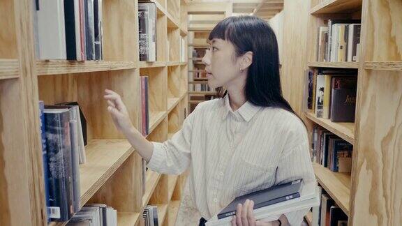 年轻可爱的亚洲女大学生在图书馆找书(慢镜头)