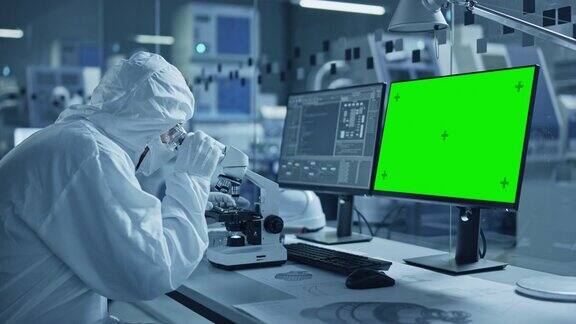 研究工厂洁净室:特写工程师科学家穿着工作服和手套使用显微镜电脑显示色度键绿色屏幕显示科学和电子研究设施