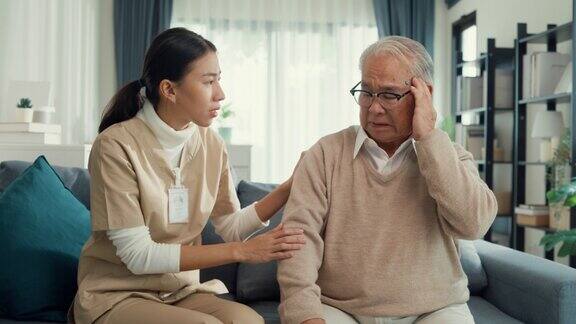 年轻的亚洲女性专业护理人员照顾触摸平静生病的老年男性病人在家里的客厅