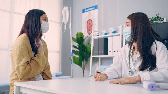 亚洲女性病人拜访年轻医生咨询健康问题在大流行期间有吸引力的治疗师在办公室医院为生病的女孩提供治疗时戴着口罩