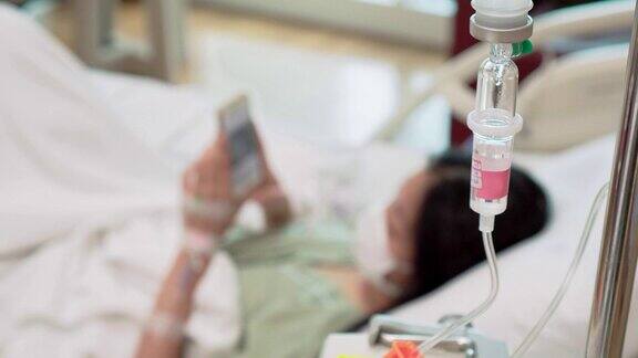 分散的亚洲年轻女子在医院的床上静脉滴注和智能手机