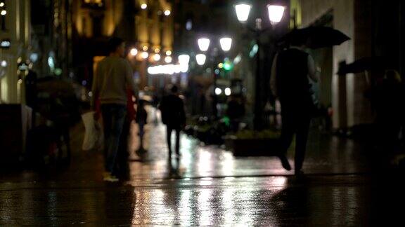 在雨夜的城市里街道上挂满了路灯柏油从雨中闪闪发光不认识的行人年轻人现代都市夜生活生活方式汽车和行人