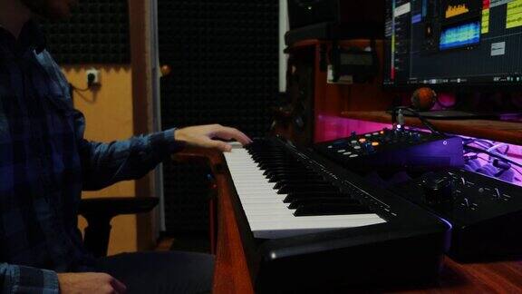 年轻的音乐家弹奏钢琴midi键盘在家庭录音工作室音响工程师录制音乐监视器和均衡器混音装置在屏幕上作曲家混合和掌握流行摇滚的轨道