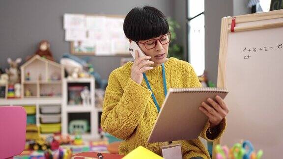 年轻的中国女幼儿园老师在幼儿园用智能手机阅读笔记本