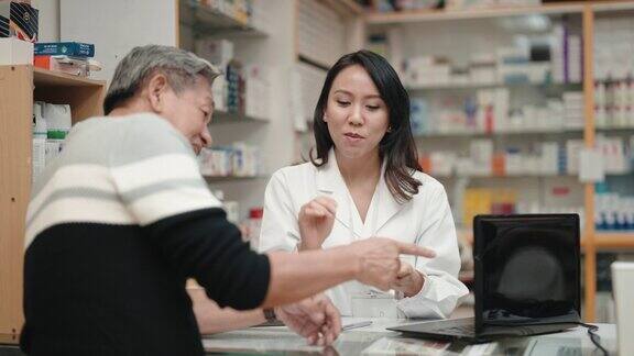 亚洲华裔女药剂师在药房柜台向年长的男性顾客解释