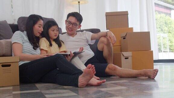 快乐的亚洲年轻家庭业主买了新房中国妈妈、爸爸和女儿抱着箱子一起坐在地板上期待着搬家后的新家的未来