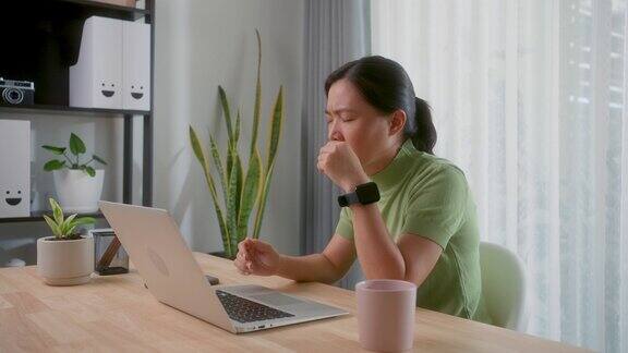 一名在手提电脑前工作的亚洲妇女发烧、流鼻涕、鼻塞和喉咙痛