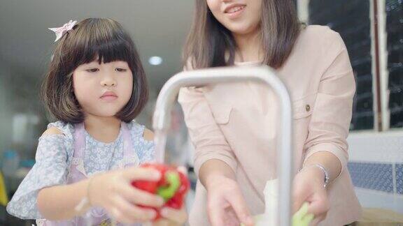 亚洲母亲教女儿在厨房里清洗和切菜家庭