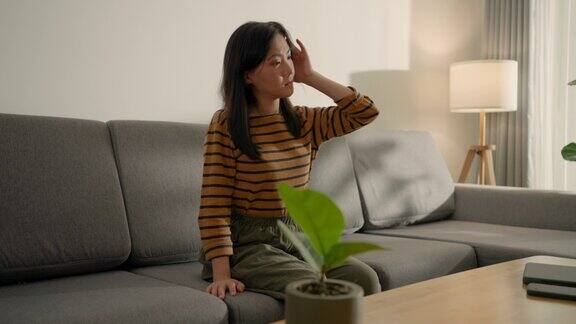 一位亚洲妇女坐在家里客厅的沙发上头痛得很厉害