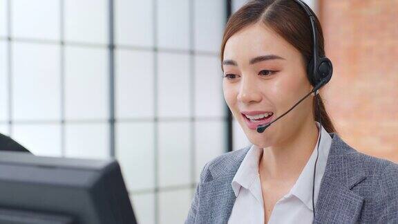 亚洲女性呼叫中心客户服务电话销售在正式的西装戴耳机或耳机与客户在现代办公室谈话