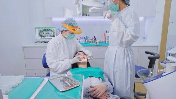 亚洲女牙医穿着实验服戴着防护面罩和护盾为小女孩病人调整牙科椅和检查牙齿协助和调整牙科手术光源
