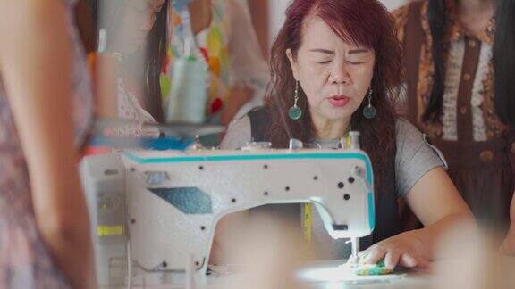 亚洲华人高级妇女裁缝教学展示她的学生在缝纫课在工作室工作坊