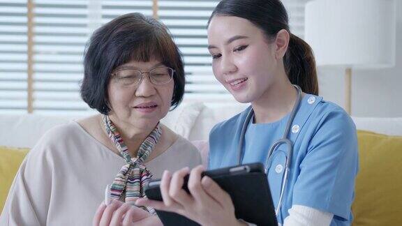 年轻的亚洲女性护士辅助生活家庭护理员或医生在家里拜访老年人在平板电脑上在线谈论结果跟踪检查表保健建议或处方
