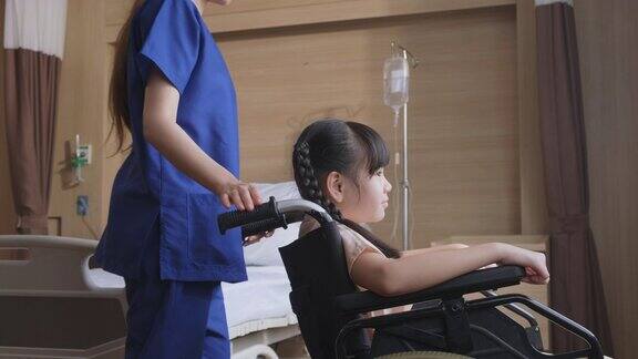 亚洲擦洗女护士照顾女孩小孩病人坐在轮椅上在医院恢复室身着制服的女医务人员推着轮椅来到窗前微笑着和小女孩交谈