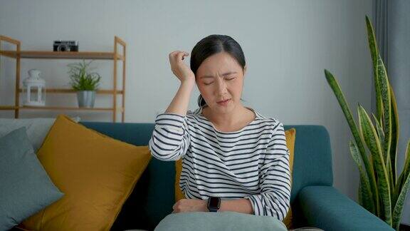 一位亚洲妇女坐在家里客厅的沙发上患了头痛