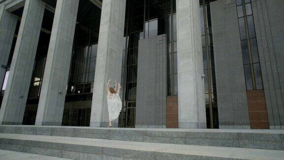 身穿白裙的年轻舞者在户外慢动作摆腿芭蕾舞女演员在石柱建筑群的画廊里跳舞4kProresHQ120fps