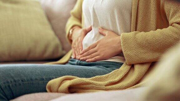 痛经、经期和女性用手捂胃用于月经周期、怀孕或腹部绞痛健康消化问题和女孩在沙发上抱着腹部子宫内膜异位症经前综合症和疼痛在家里
