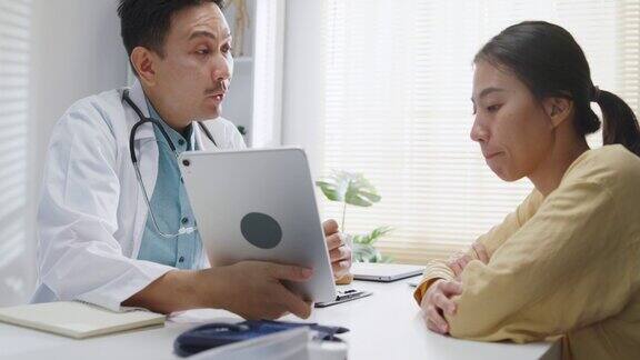 成熟的亚洲男性医生在健康门诊用平板电脑与女性患者会诊时的医疗结果