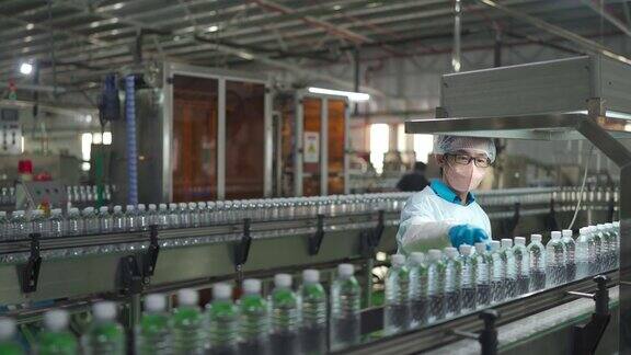 亚洲华人男性生产线工人携带个人防护装备检查瓶装水厂的水瓶