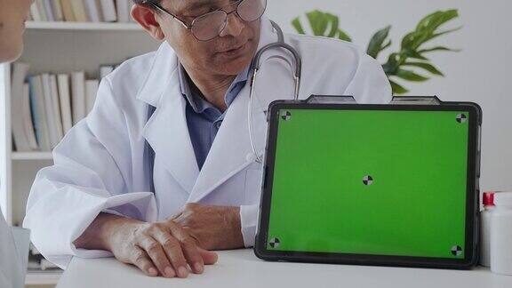 资深医生在诊所用绿屏平板电脑向病人讲解