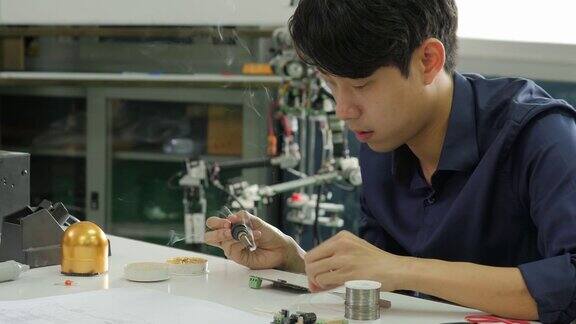 一位亚洲电子工程师正在他的车间里焊接一块电路板亚洲学生正在教室里学习电子学和焊接