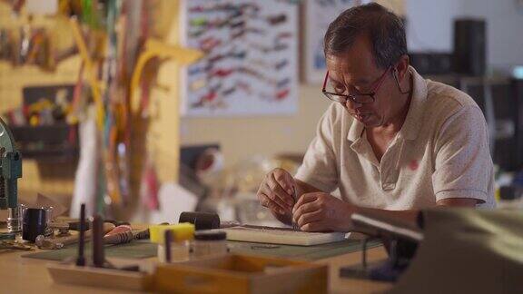 一位亚洲华人老人在他的工作室里制作手工皮革表带