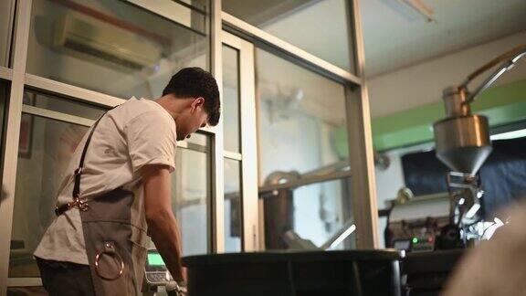 亚洲华人男工人将生咖啡豆从桶中舀到秤机上并将其混合在工厂仓库的咖啡烘焙过程中