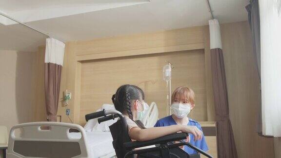 亚洲擦洗制服护士照顾女孩小孩病人坐在轮椅上在医院恢复室年轻妇女和儿童佩戴外科口罩以预防covid-19大流行