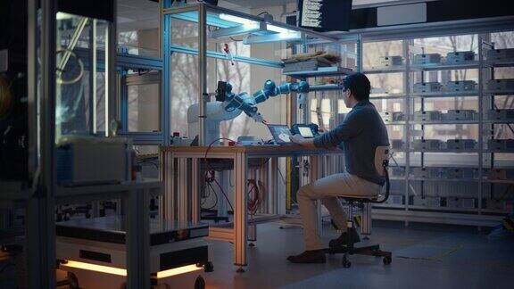 年轻的专业开发人员在笔记本电脑上编程在工厂车间操纵机器人手臂设计自动化机器人系统的人创业