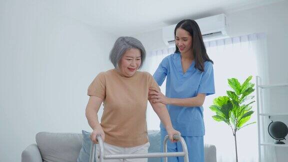 亚洲老年妇女病人做物理治疗与照顾者有吸引力的专业护理人员帮助和支持老年成熟的祖母实践行走缓慢与步行者在养老院照顾
