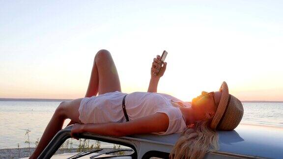 女孩手拿手机躺在车顶上在手机上拍下女孩在夕阳下的照片