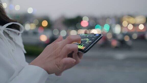 夜晚灯光模糊的城市街道上女性手握手机浏览互联网的特写