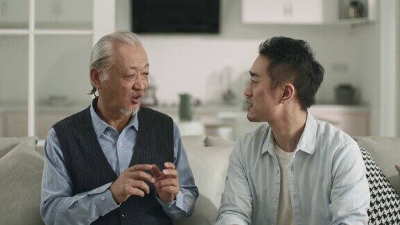 年长的亚洲父亲和成年的儿子在家里聊天