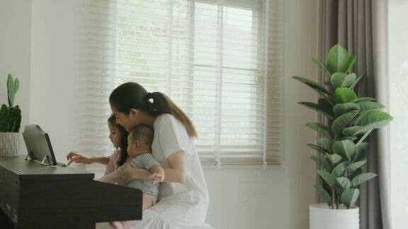 快乐的时光妈妈和她可爱的孩子在家弹钢琴音乐训练有助于培养婴儿的大脑手眼协调能力增强的明显迹象