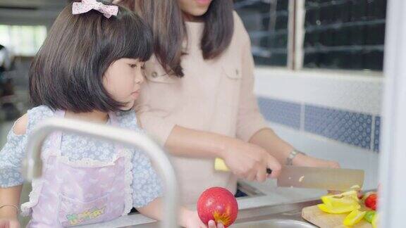 亚洲母亲教女儿在厨房里清洗和切菜家庭