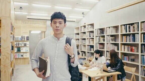 一个年轻的亚洲男学生站在图书馆的肖像