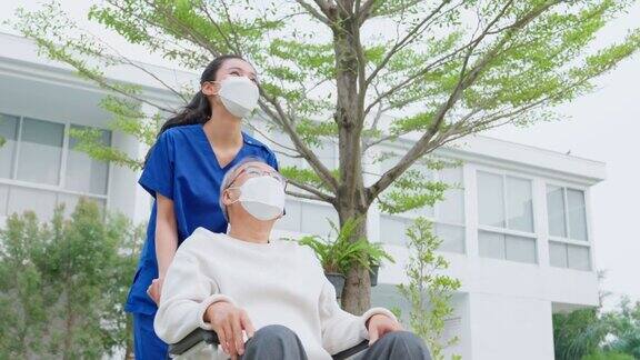 亚洲护理护士在户外照顾坐在轮椅上的老年男性美丽的专科女孩医生帮助和支持老年成熟的老年病人男子在公园做物理治疗在流行病期间