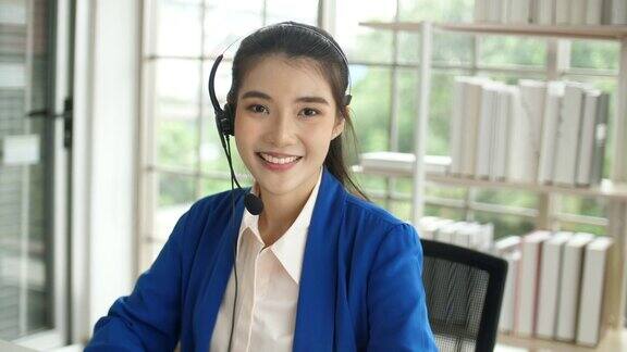 美丽的女性呼叫中心工作戴着耳机支持客户看着相机