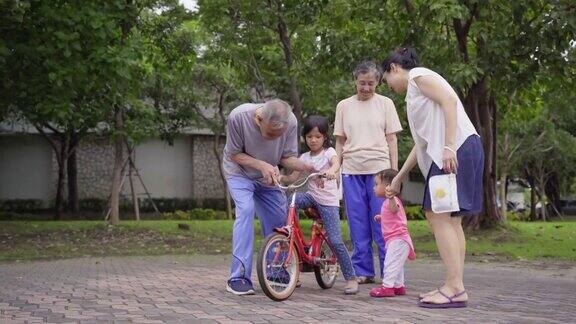 爷爷在和家人散步的时候帮孙女学骑自行车