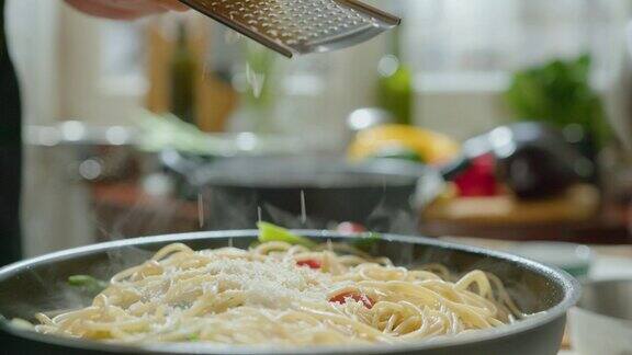 在煎锅中煮熟的意大利面上磨碎奶酪