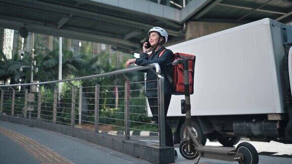 亚洲华人女性快递员在城市以电动滑板车为交通工具在移动中检查订单地址