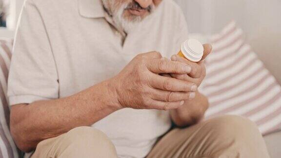亚洲老人独自坐在家里看着一瓶药生病的亚洲老人拿着药在家里的客厅里