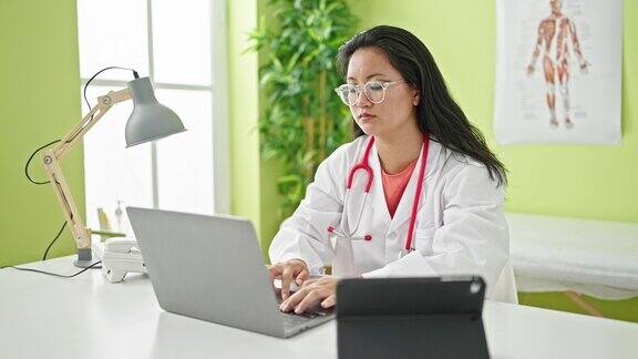 年轻的中国女医生使用笔记本电脑和触摸板在诊所工作
