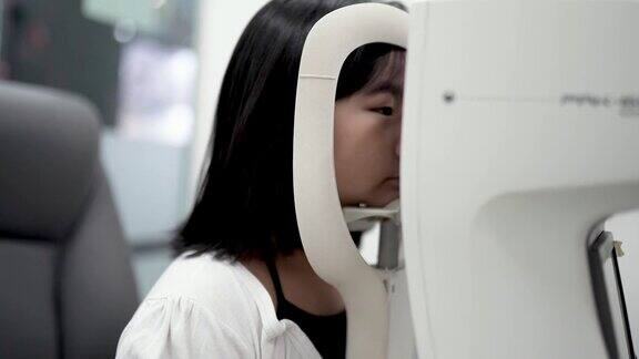 在眼科诊所亚洲华人女孩坐在椅子上用数码相机做视力测试