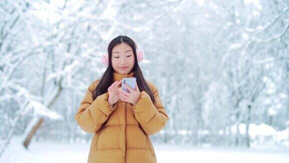 快乐快乐有趣的亚洲少女学生在一个下雪的冬天在公园里散步听音乐有手机的年轻女子喜欢在寒冷的天气里跳舞