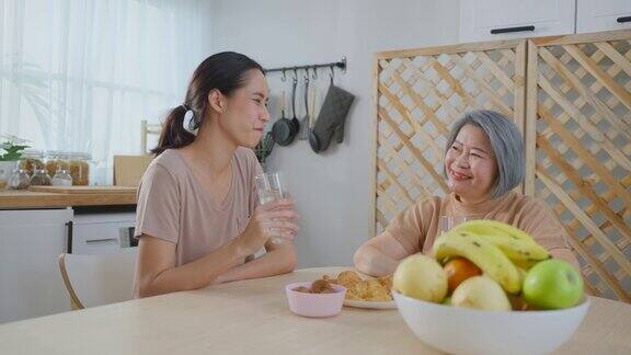 亚洲年轻迷人的女儿吃早餐与资深母亲漂亮的女孙女坐在家里厨房的桌子上烤羊角面包端给年迈成熟的奶奶吃