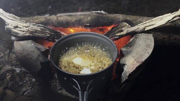 在露营地的火炉上用野地锅煮方便面和鸡蛋篝火做饭旅游和露营露营时的深夜晚餐