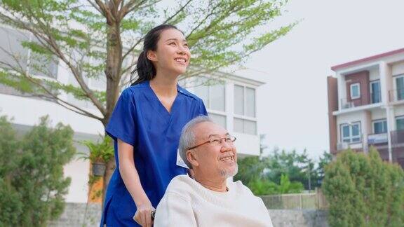 亚洲护理护士在户外照顾坐在轮椅上的老年男性美丽的专科女医生帮助和支持老年人成熟的老年病人男子在疗养院公园做物理治疗